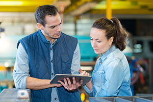 Two warehouse workers look at a tablet while conducting a security audit.