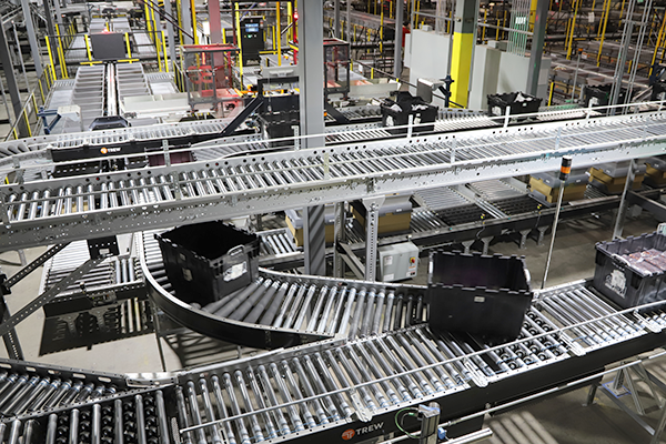 Trew automated conveyor system transporting bins in a manufacturing facility